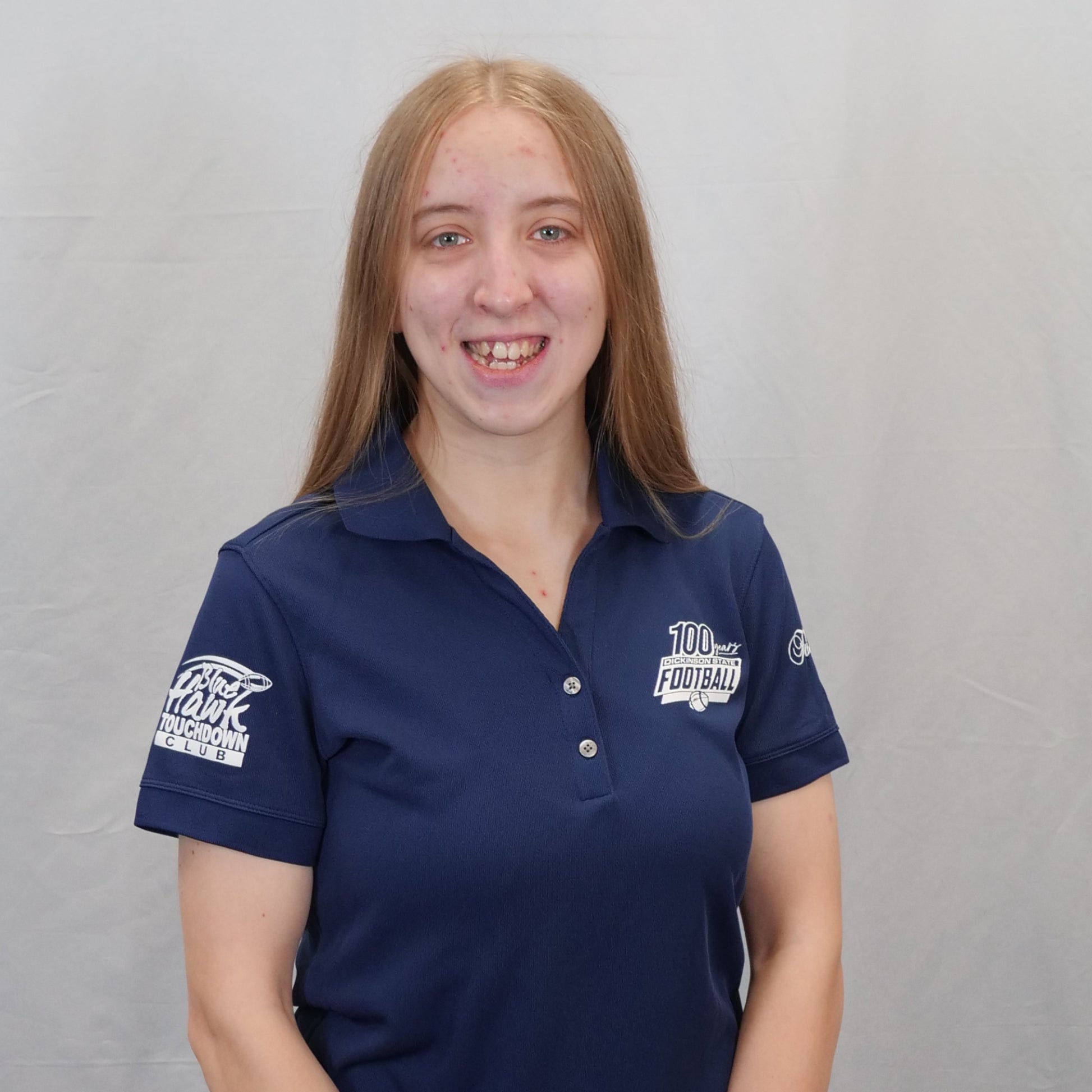 Person wearing a navy blue polo shirt with logos on sleeves against a gray background