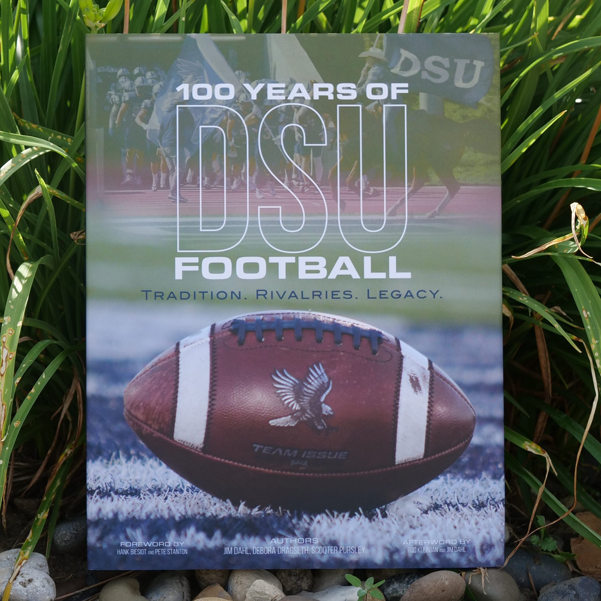 Book titled '100 Years of DSU Football' with a football on the cover, placed on grass.