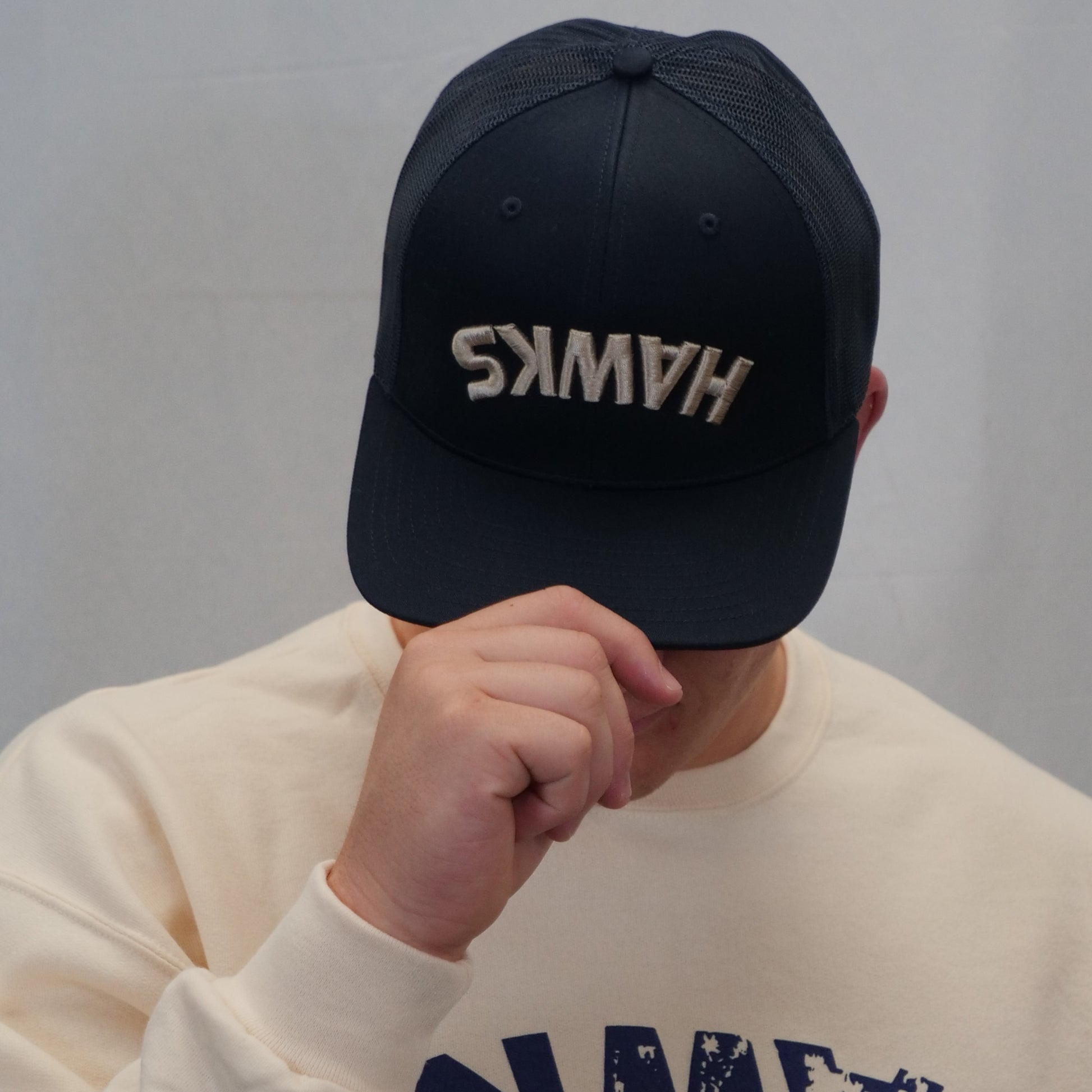 Person wearing a black cap with 'HAWKS' embroidered on it against a gray background