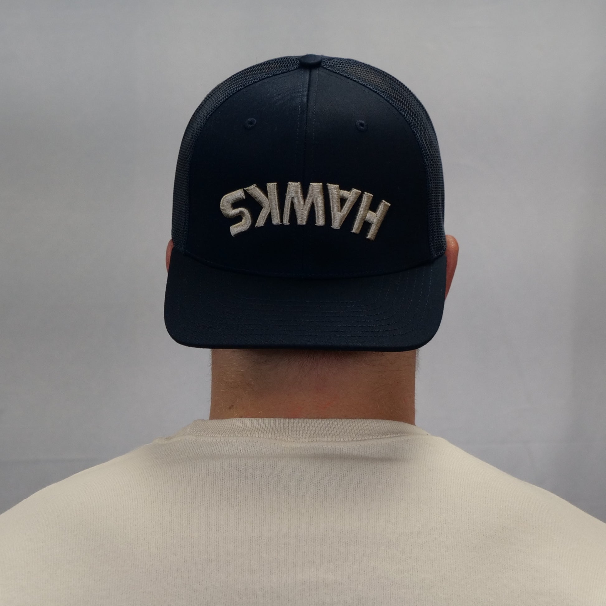 Person wearing a navy blue cap with 'HAWSS' embroidered on the back against a gray background