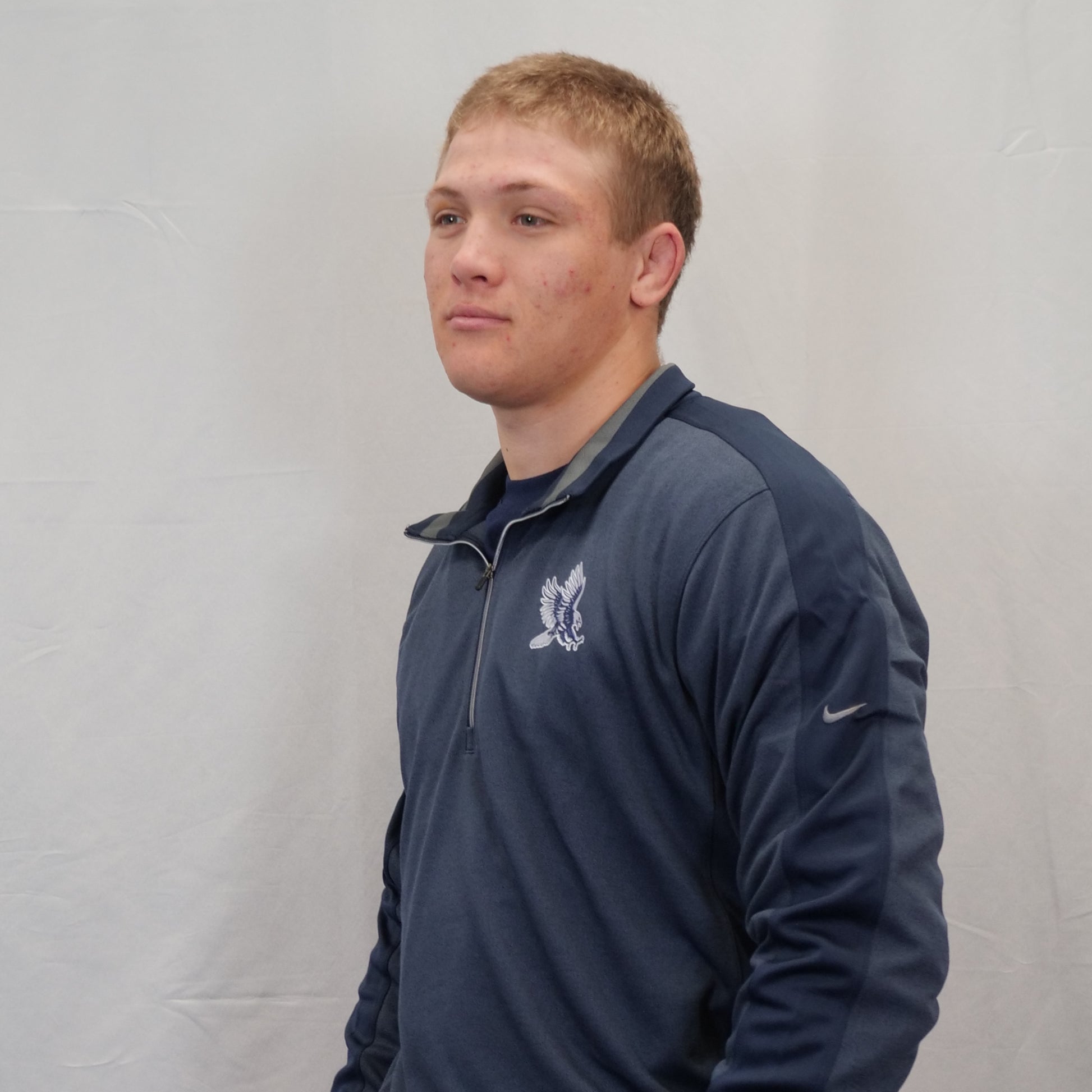 Person wearing a navy blue jacket with a logo on a plain background