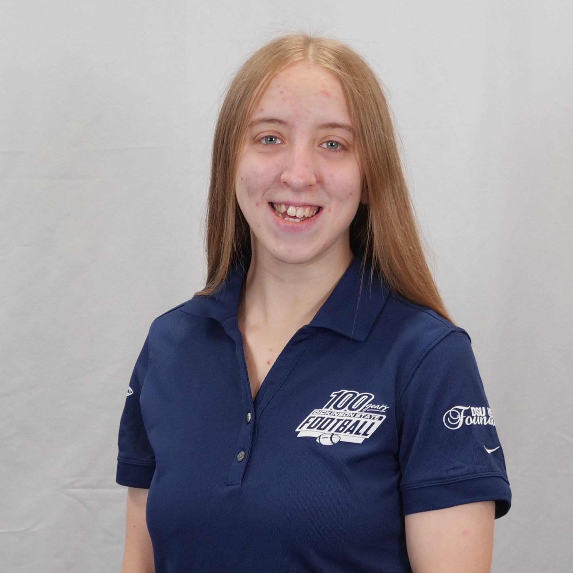 Person wearing a navy blue polo shirt with logos on a gray background