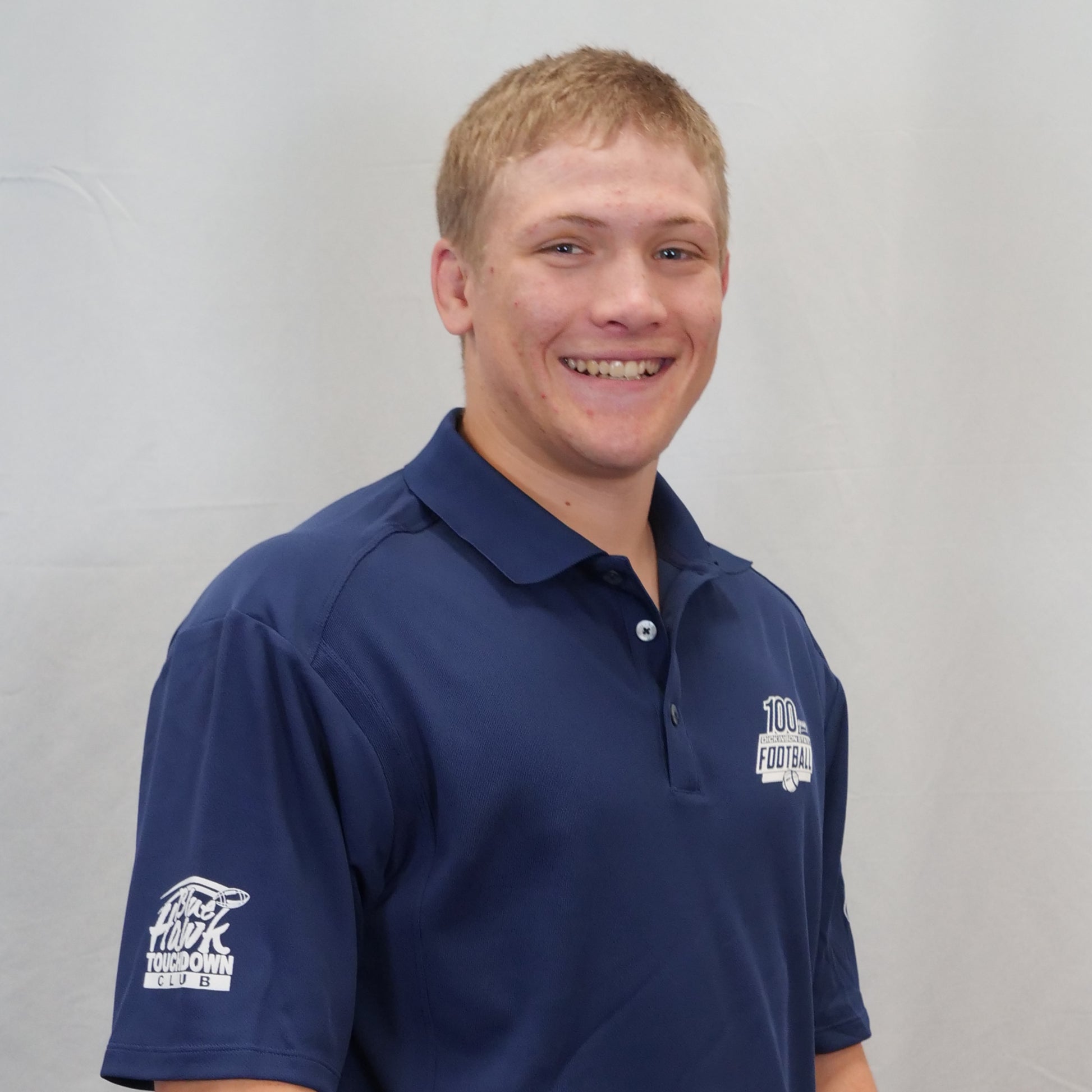 Man wearing a navy blue polo shirt with logos on a gray background