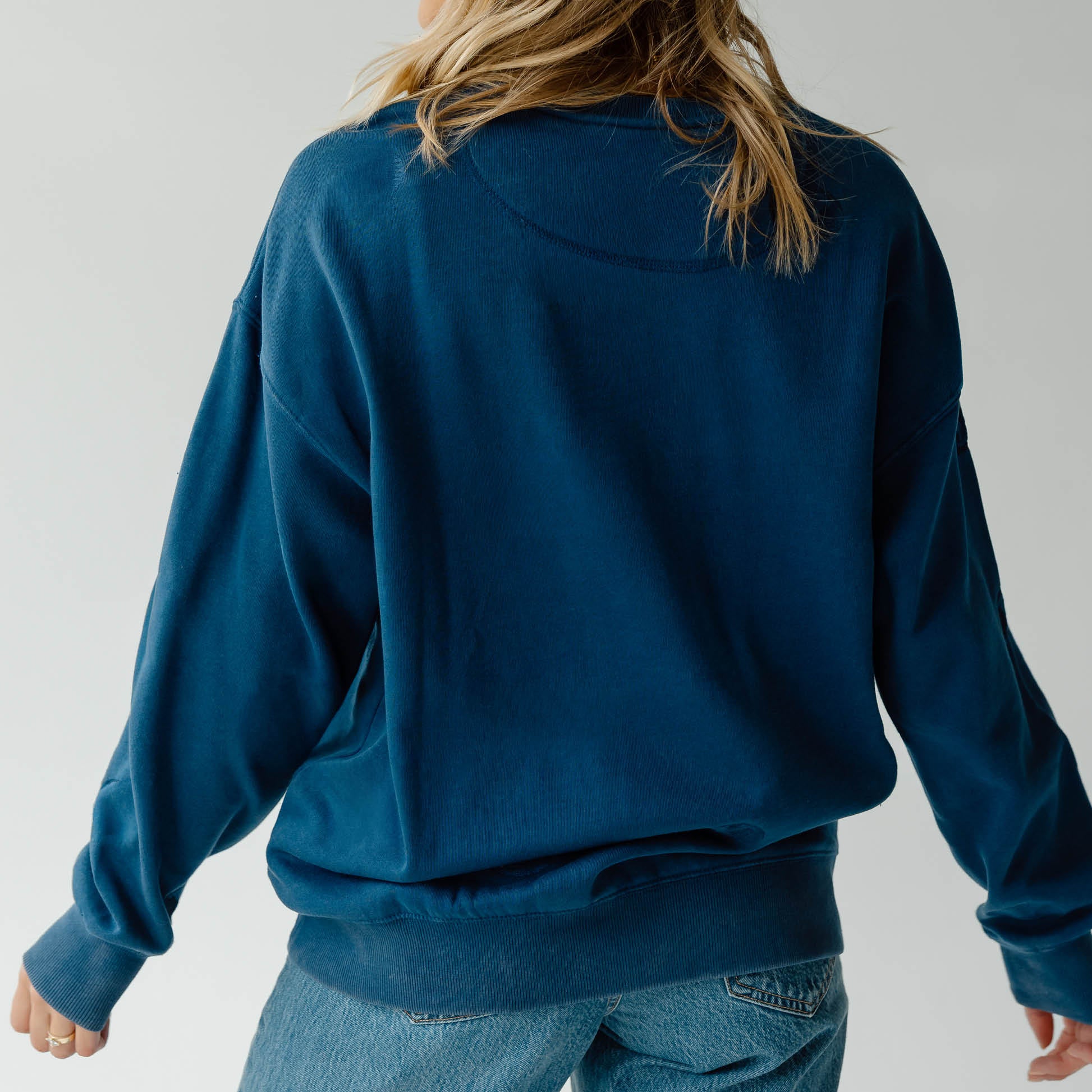 Person wearing a blue sweatshirt and jeans on a plain background