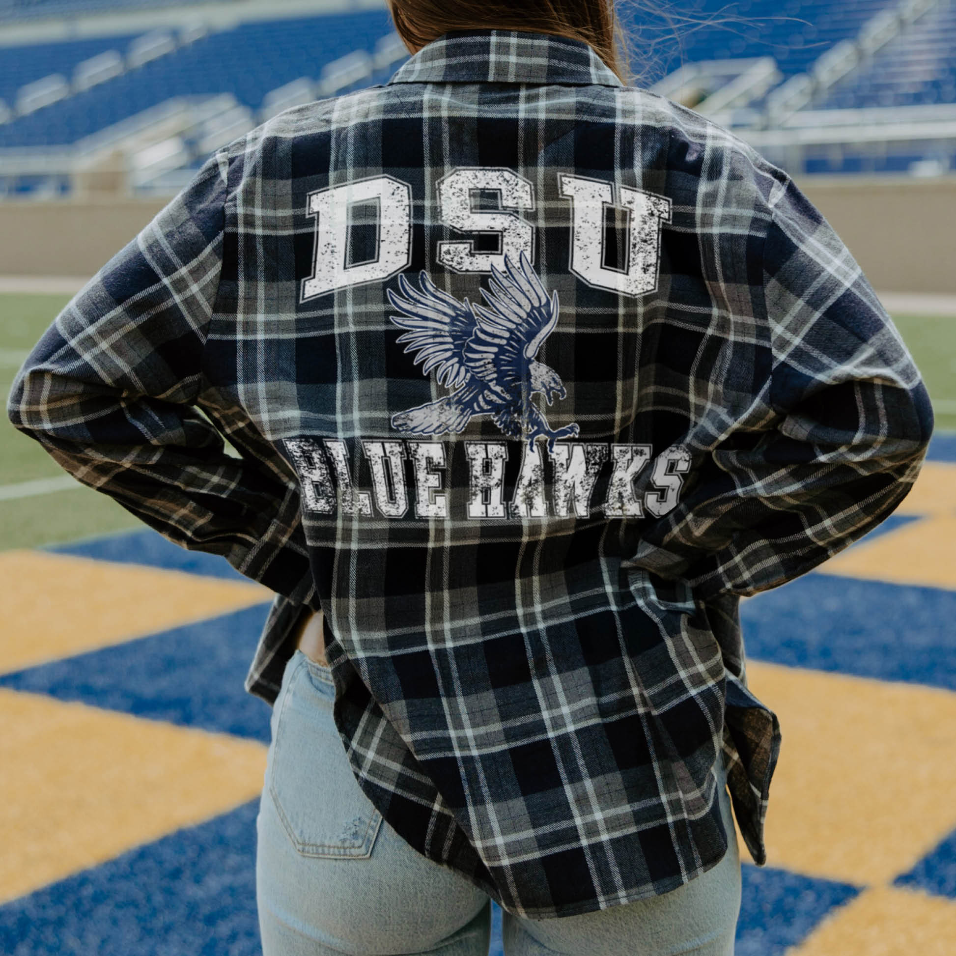 Person wearing a plaid shirt with 'DSU Blue Hawks' text and logo on a sports field.