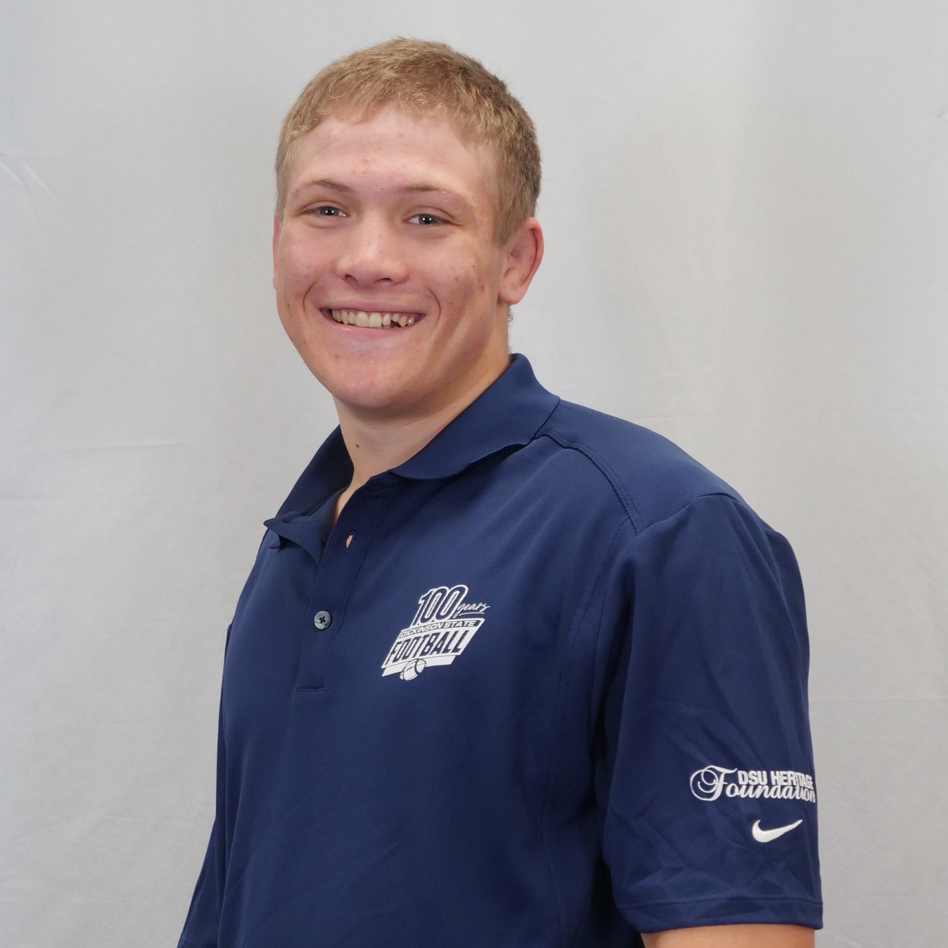 Man wearing a navy blue polo shirt with logos on a gray background