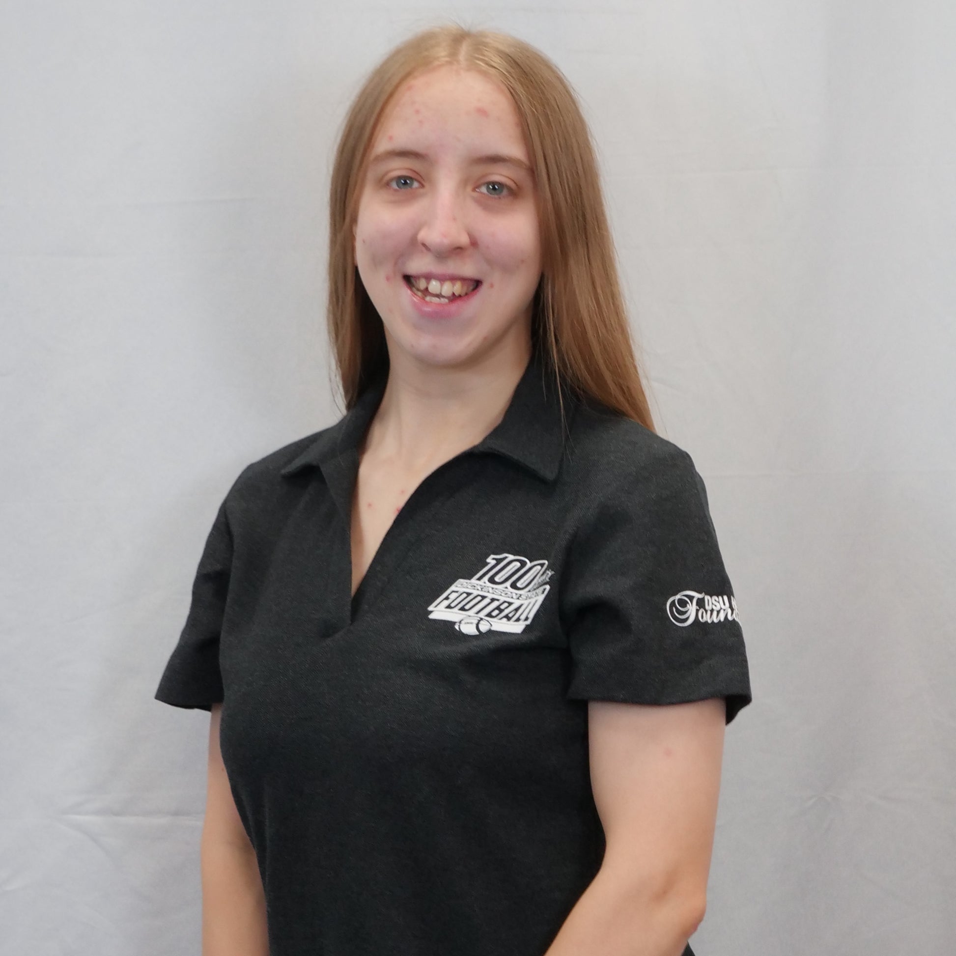 Person wearing a black polo shirt with logos on a gray background