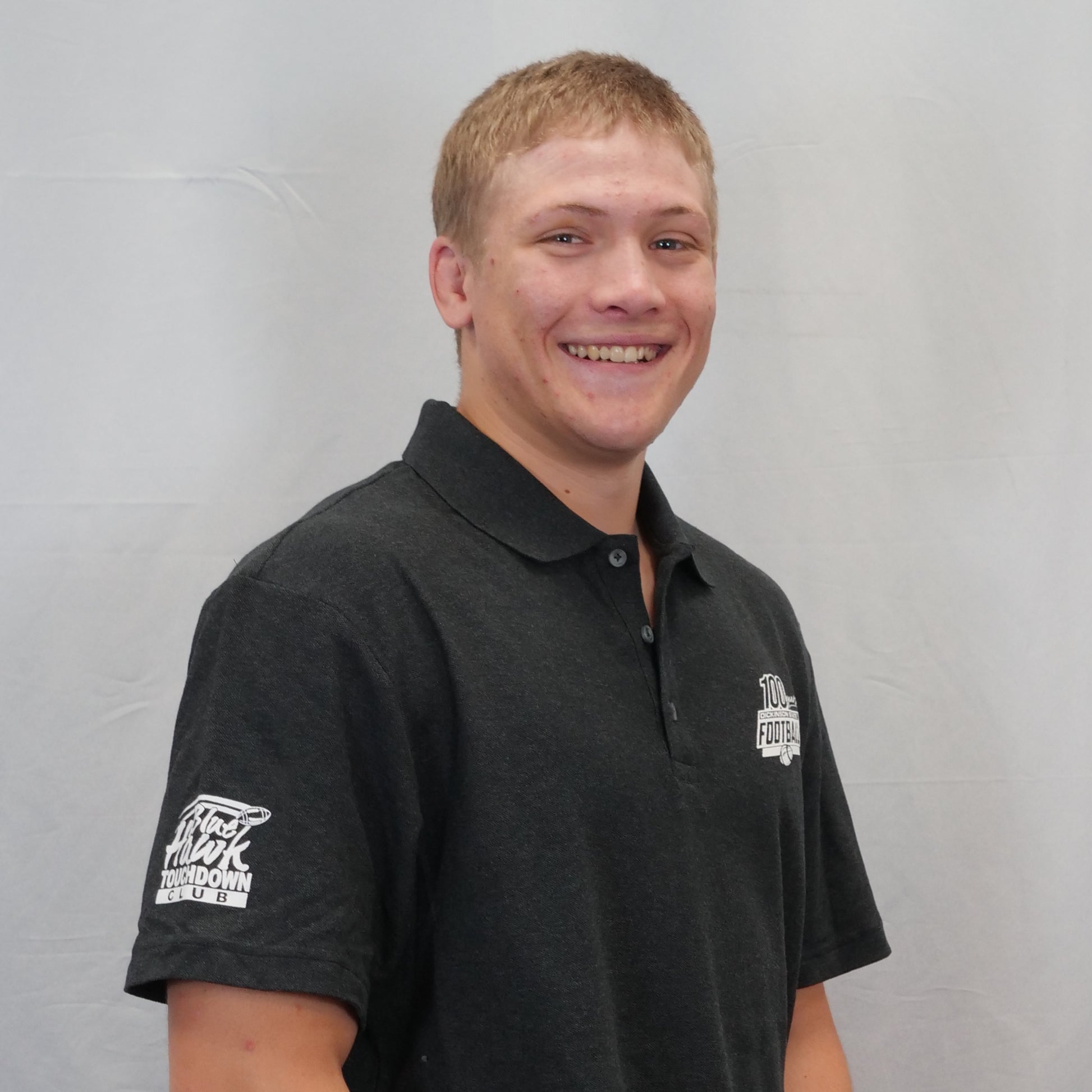 Man wearing a black polo shirt with logos on a gray background