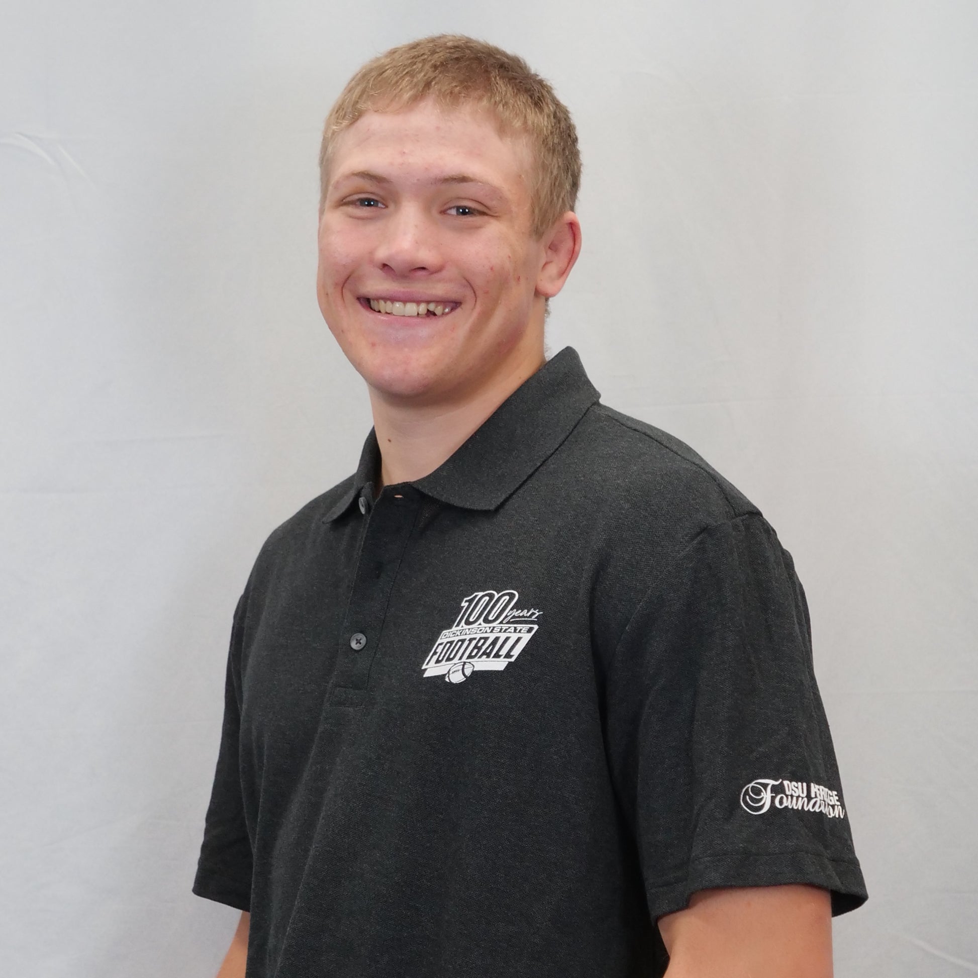 Person wearing a black polo shirt with logos on a plain background