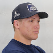 Person wearing a navy blue cap with branding on a plain background