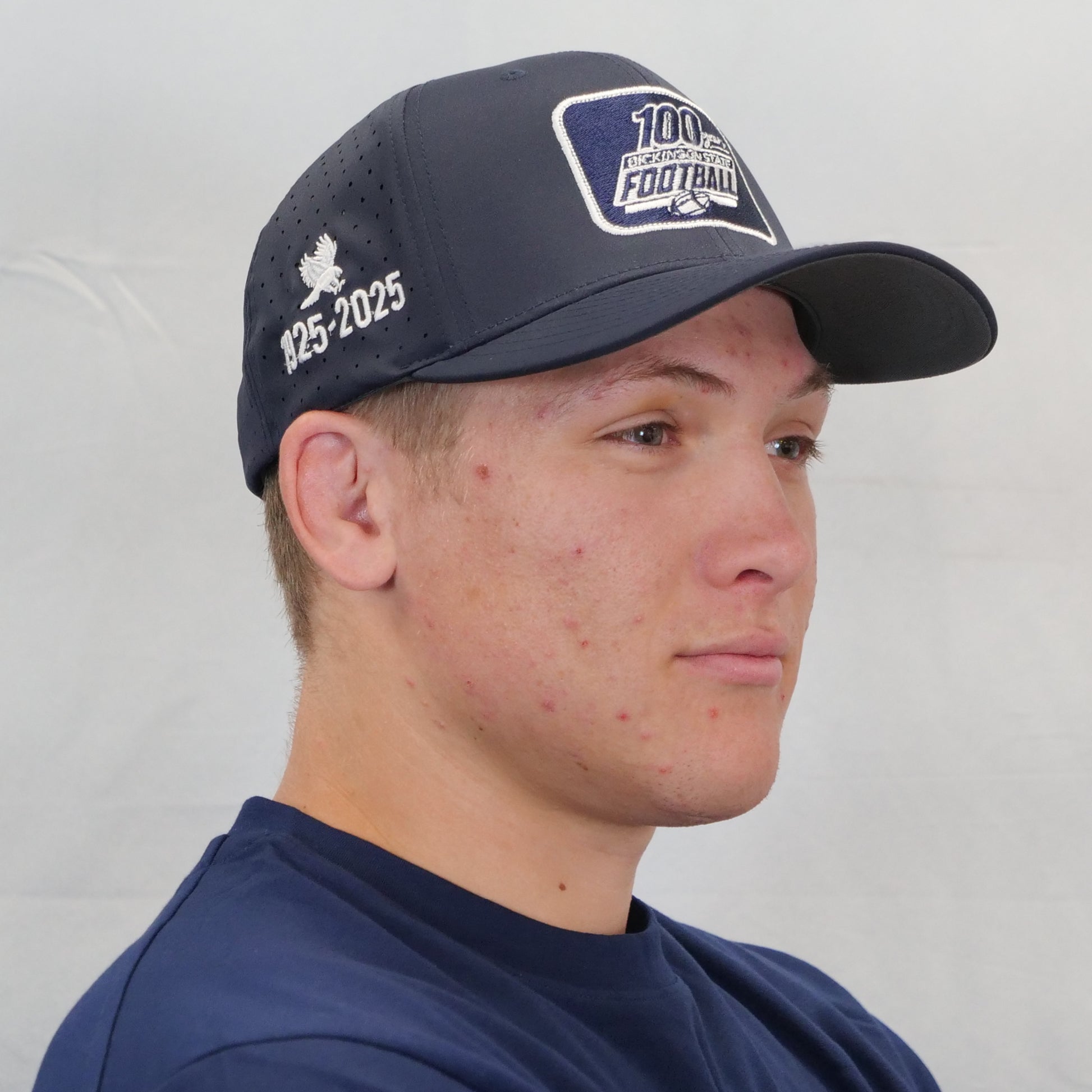 Person wearing a navy blue cap with branding on a plain background
